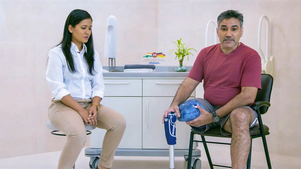 Amputee with Ottobock prosthesis sitting on a chair next to a prosthetist showing how to put on the prosthesis