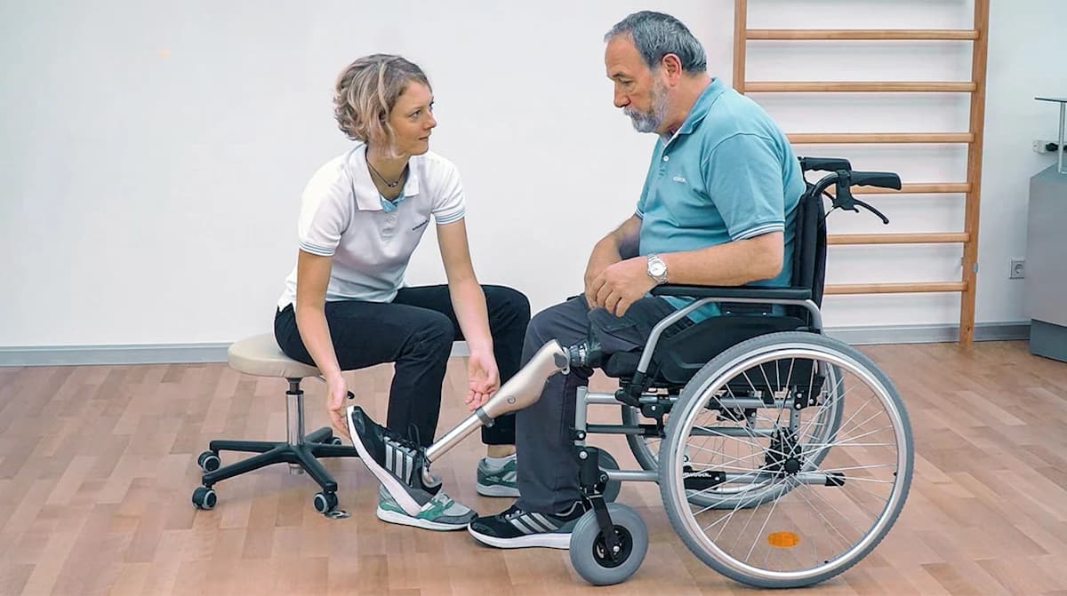 Ottobock Kenevo user sitting in a wheelchair next to a prosthetist who holds his prosthetic foot while talking to him