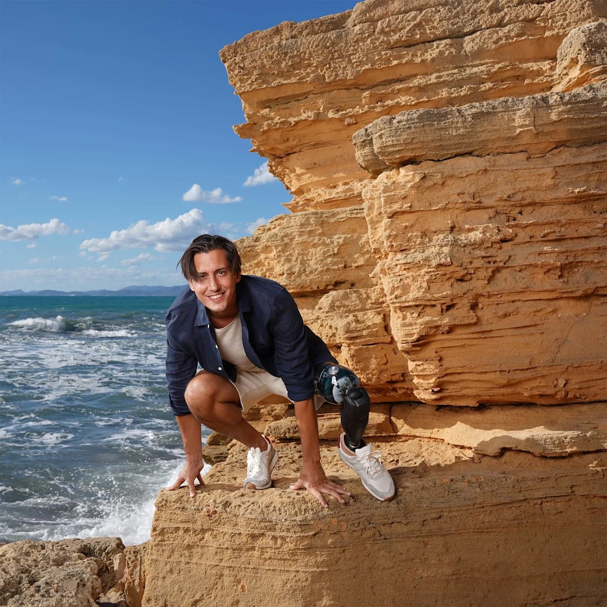 Alessandro Ossola squatting on a rock by the sea with his Evanto prosthetic foot.