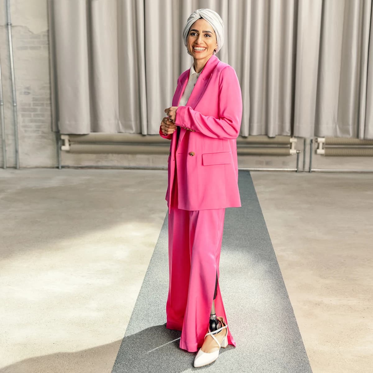 Prosthetic foot user Zainab smiles and wears a pink suit and the Ottobock Taleo Adjust with high-heeled white shoes