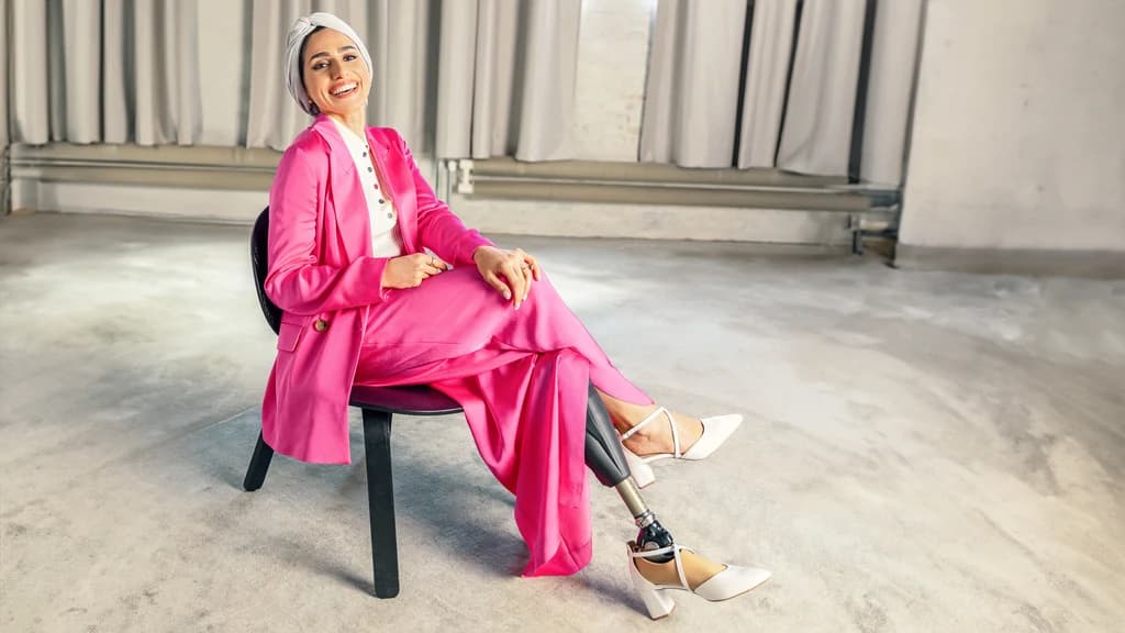 Prosthetic foot user Zainab smiles as she leans back in a chair and wears the Taleo Adjust with high-heeled shoes
