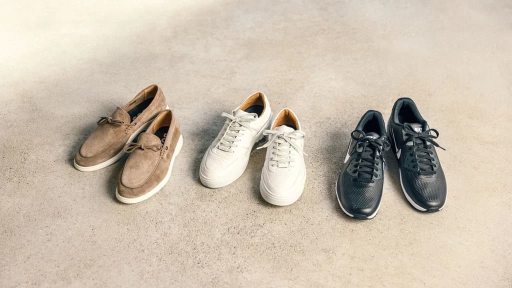 Three different pairs of shoes in brown, white and black standing on the floor