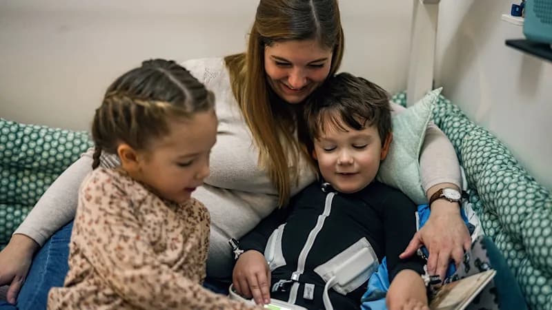 A young cerebral palsy patient cuddling with his mother and sister reading a book.