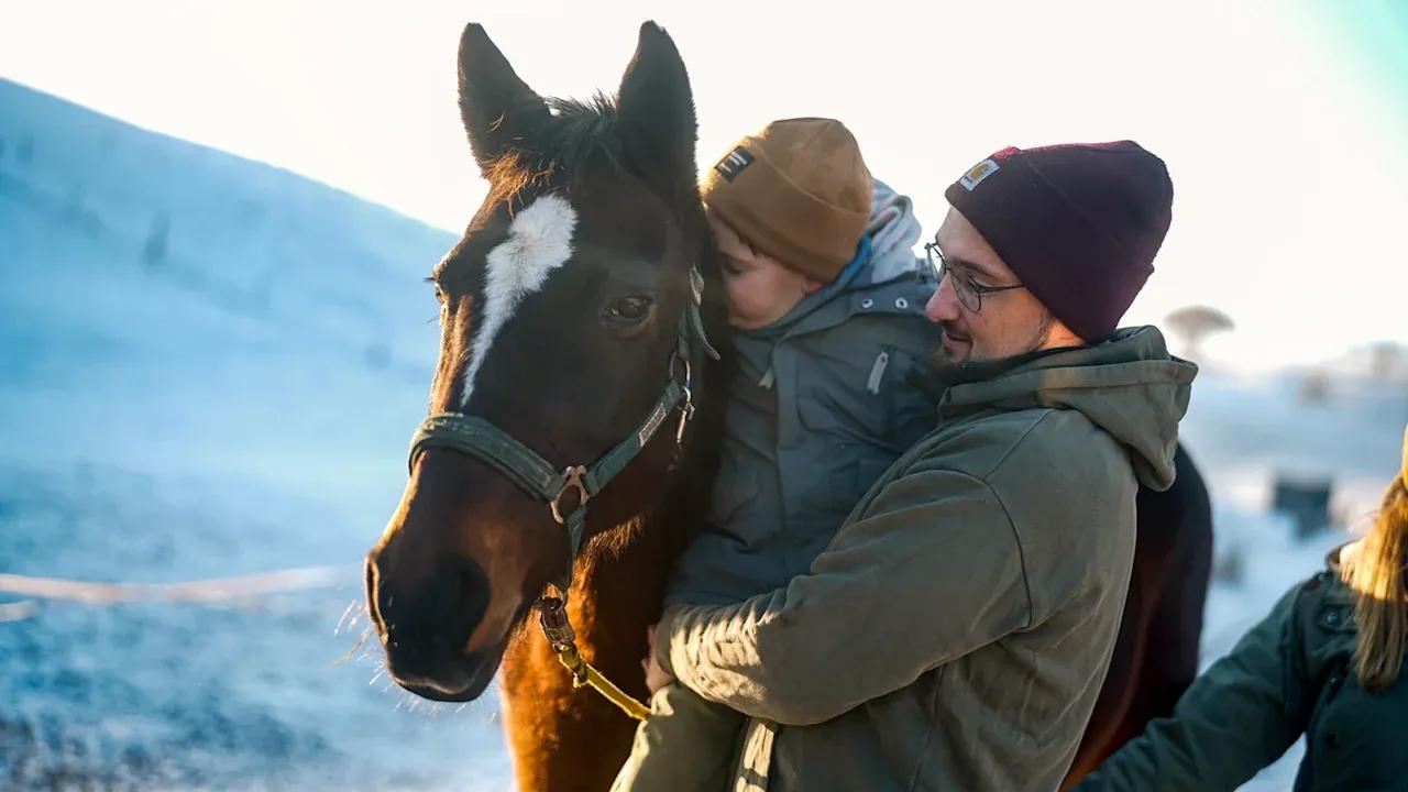 Cerebral palsy patient petting a horse together with his father.