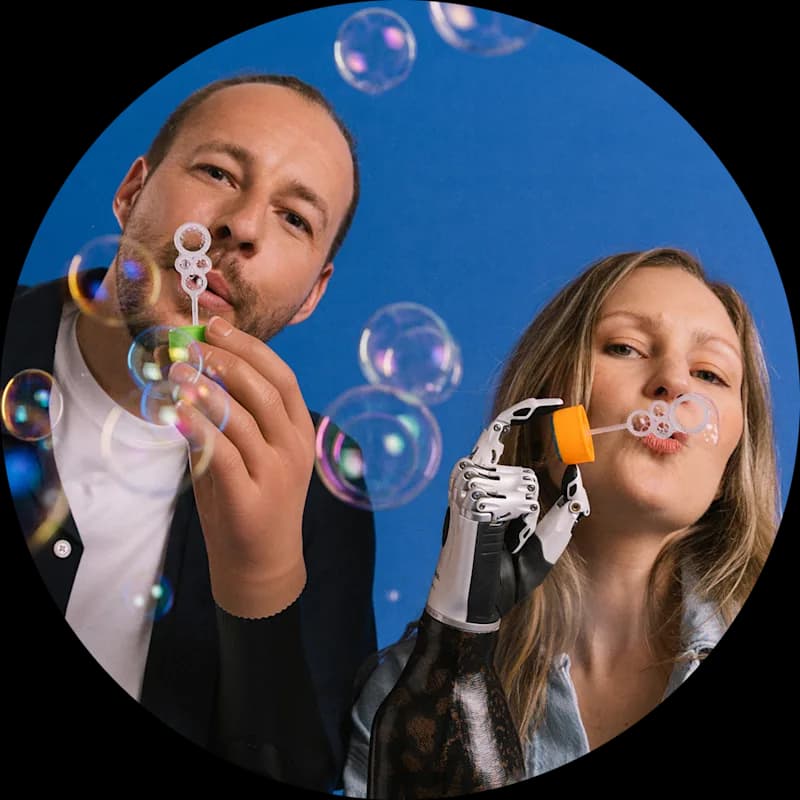 Two people blowing bubbles, one wearing a prosthetic hand.